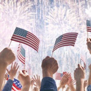 Hands wave American flags during a fireworks show.