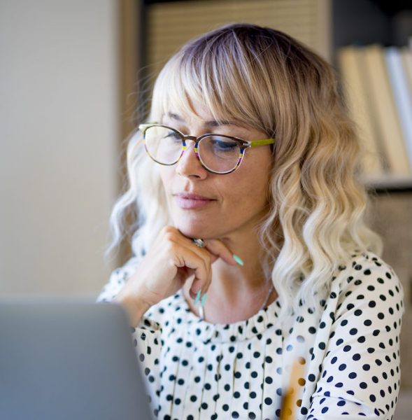 Business woman long hair glasses laptop contemplating purchasing affordable hearing aids