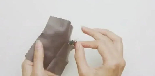 A hand uses a cloth to clean a Phonak hearing aid.