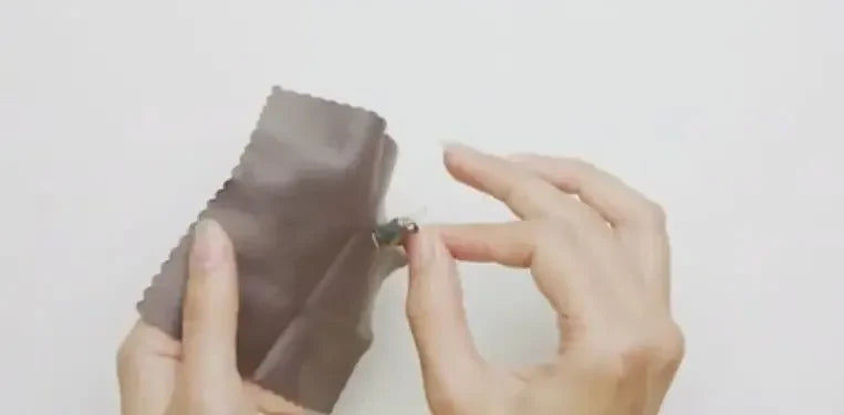 A hand uses a cloth to clean a Phonak hearing aid.