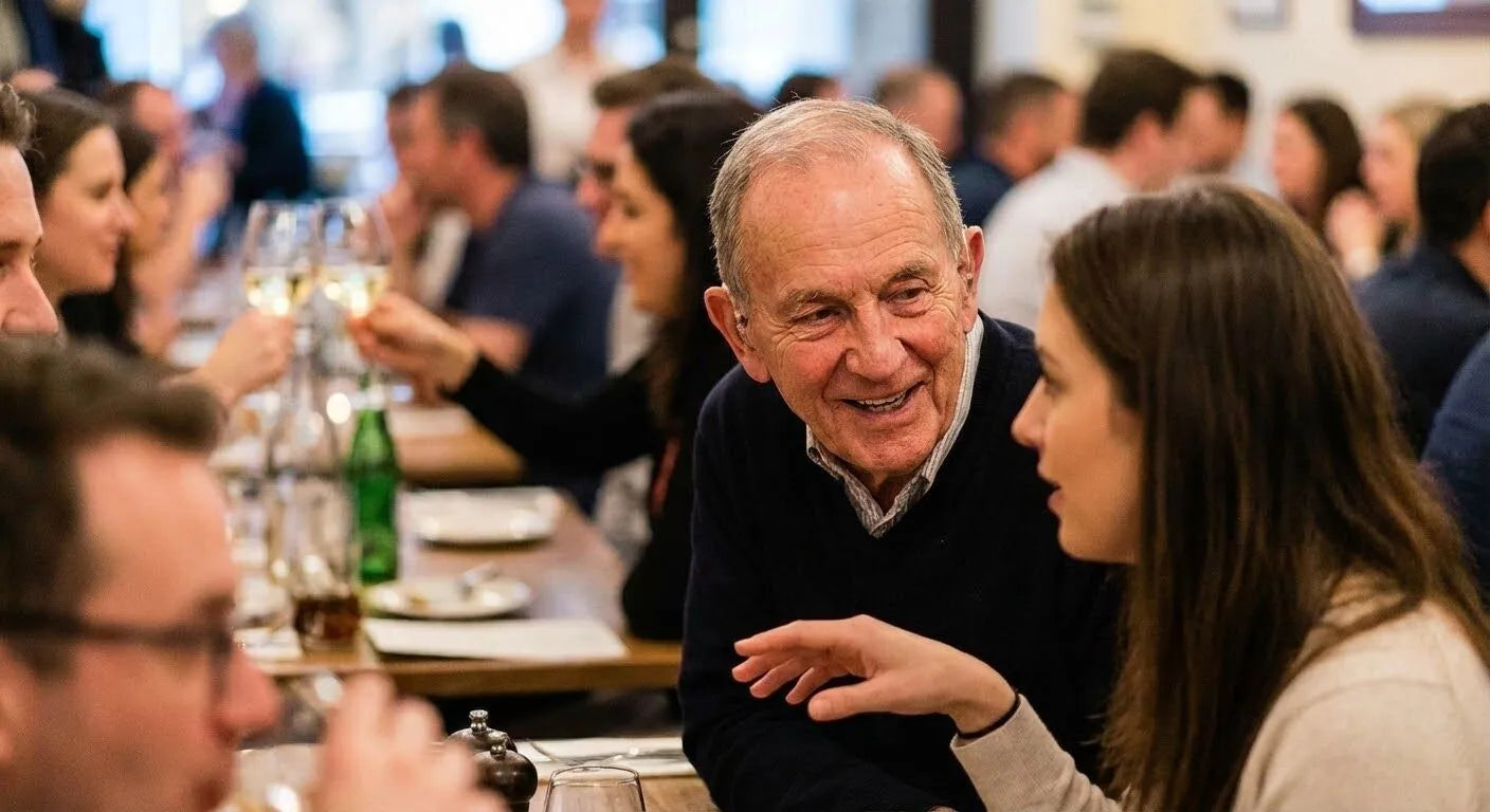 Two people engaged in conversation at a social gathering with other attendees in the background.