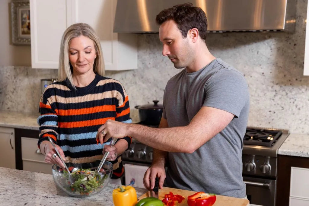 Man and woman preparing a salad together in a kitchen.