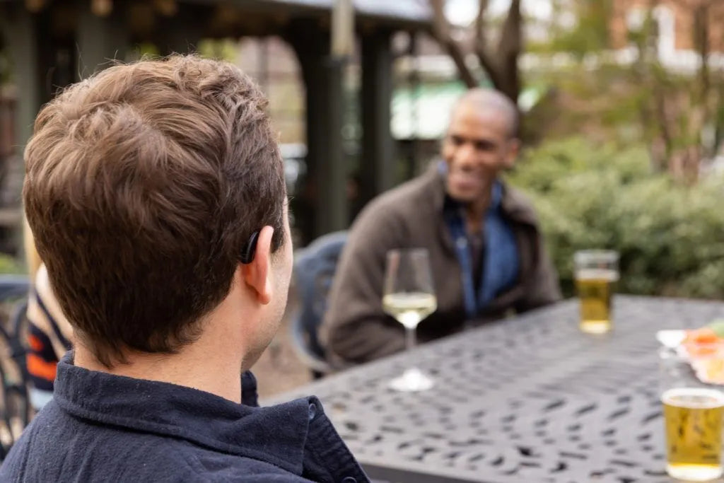 Two men sitting at an outdoor table with drinks, engaged in conversation.