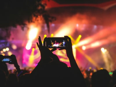 Person taking a photo of a concert with a smartphone, surrounded by colorful lights.