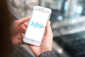 Person holding a smartphone with 'Injoy' app displayed, blurred indoor background