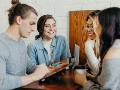 Group of four friends gathered around a table, smiling and interacting in a meeting.