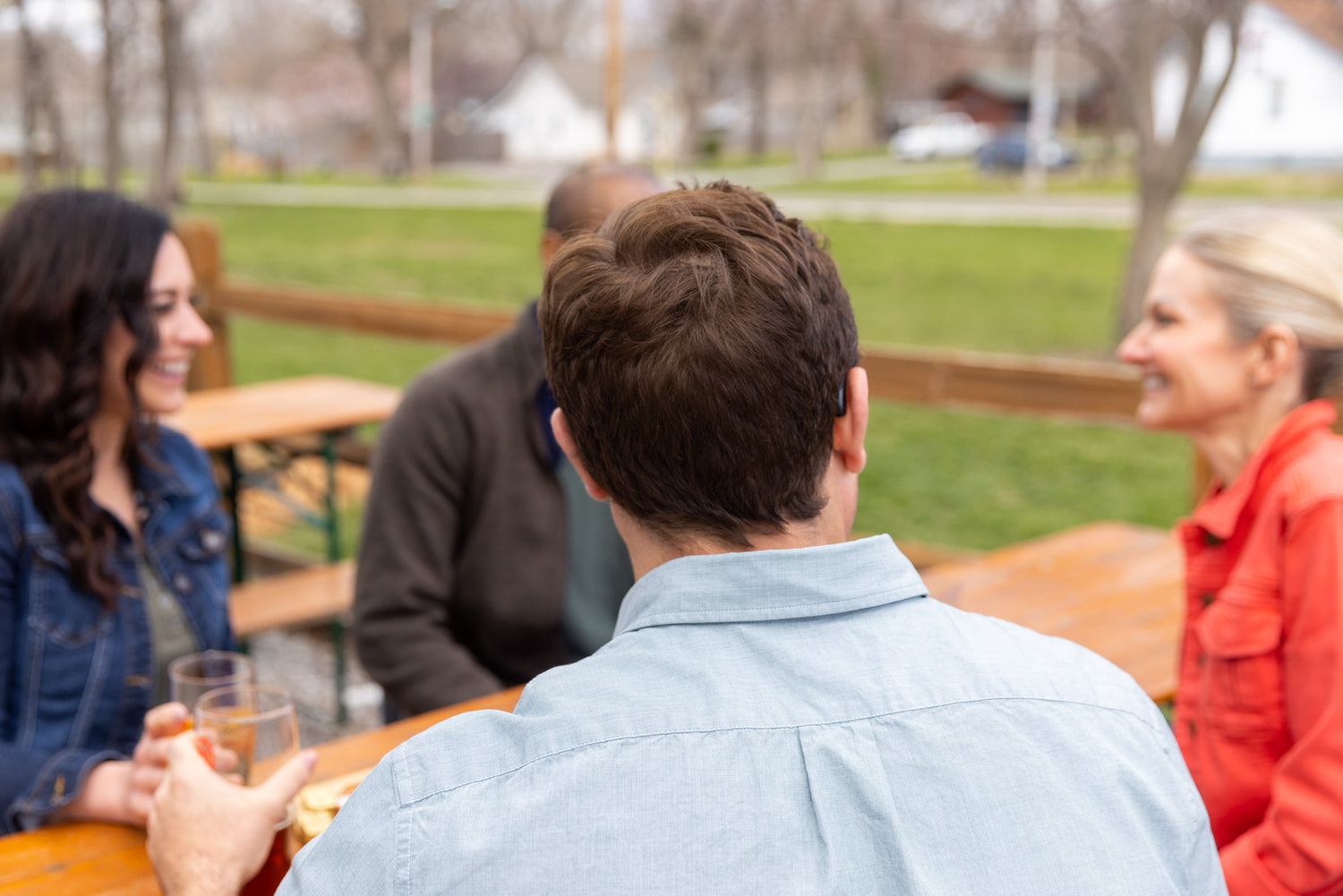 Man with hearing aid and people sitting at an outdoor table in a park-like setting