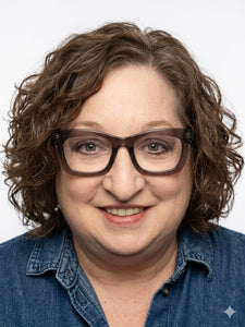 Jen Zimmerman wearing glasses and curly hair wearing a denim shirt 