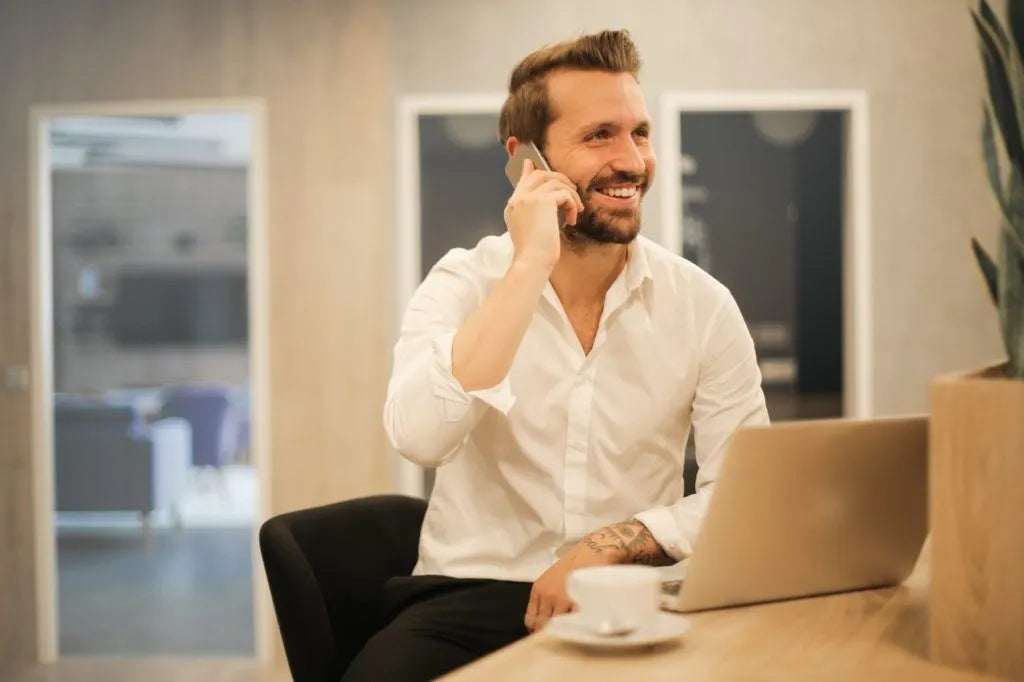 Man sitting at a desk with a laptop, talking on the phone in an office setting.