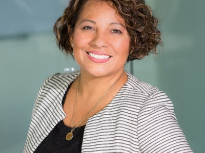 Woman with short curly hair wearing a black and white striped jacket against a blurred background