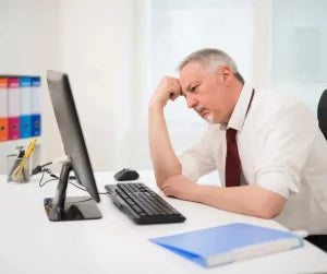 An unhappy man sits at his desk at work. 
