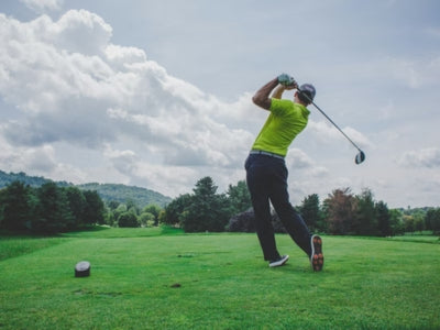 Golfer in action on a golf course with trees and clouds in the background