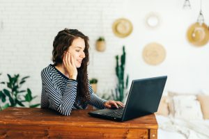 Woman using a laptop on a wooden desk in a home setting with plants and decor.