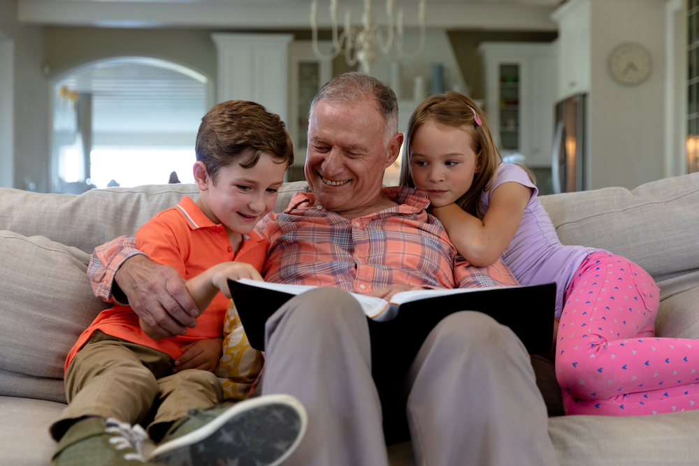 Low angle front view of a senior Caucasian man reading to grandchildren thinking do i need a hearing aid