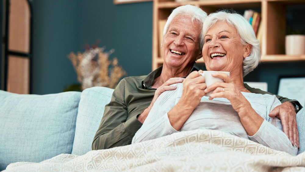 senior couple relax on sofa drinking coffee and watching comedy movie on television with their 30 day free trial hearing aid