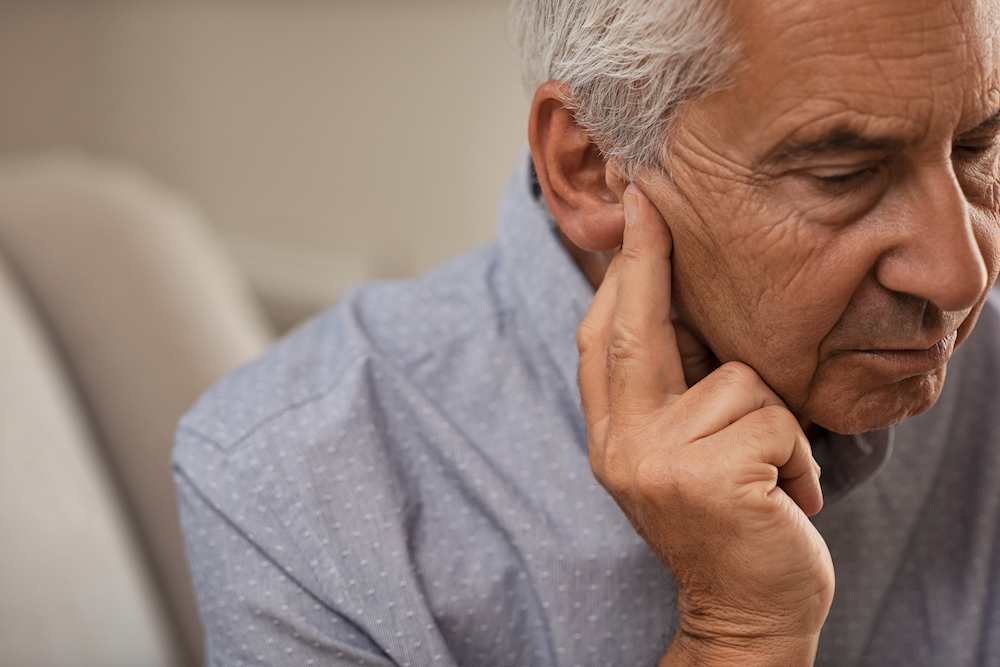 mature man holding fingers to his ear side view pain from invisible hearing aids
