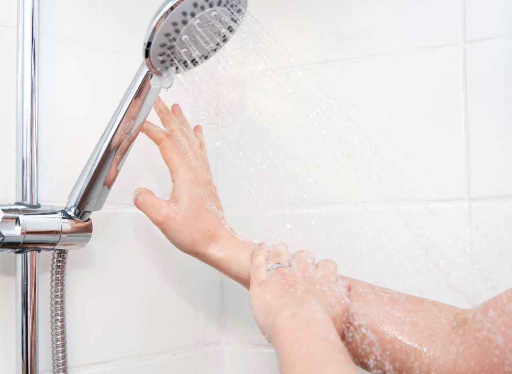 a shower head and hands using soap showing can you wear hearing aids in the shower