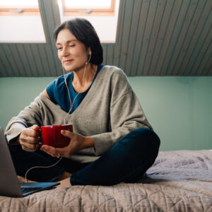 woman on bed with headphones and tea happy after answering where do I get a hearing aid