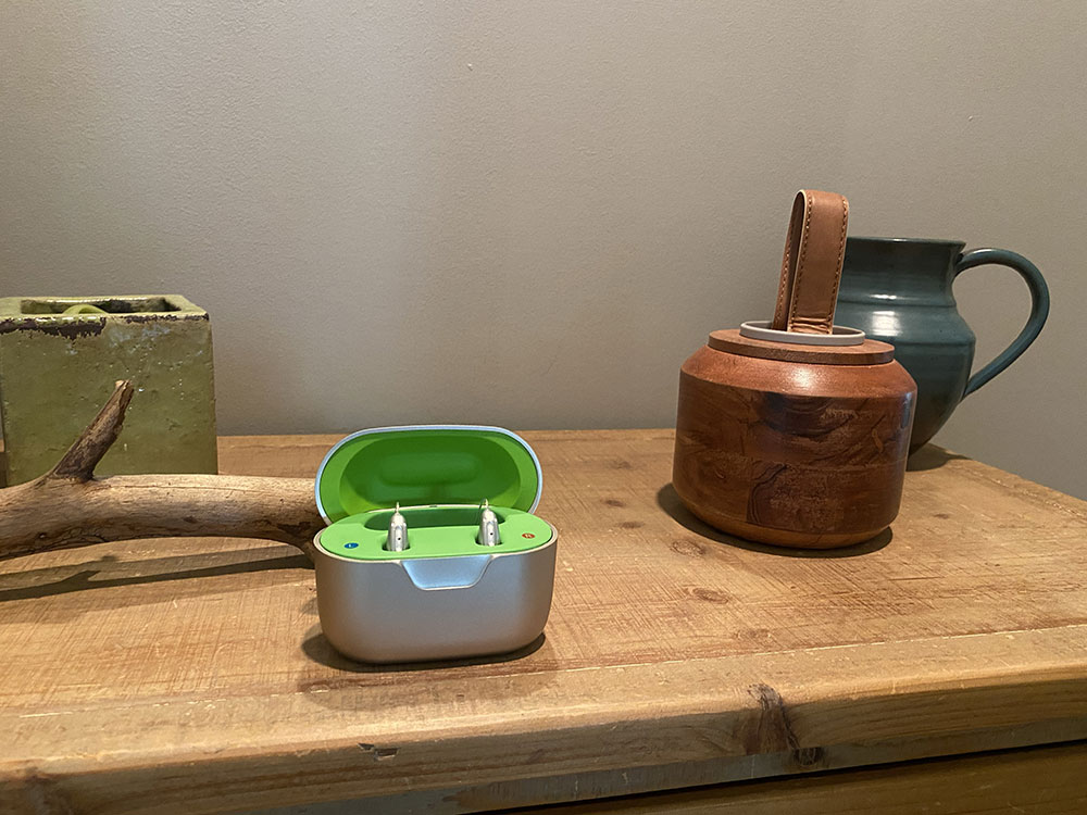 Phonak Bluetooth hearing aids sit in their charging case on a bedroom table.