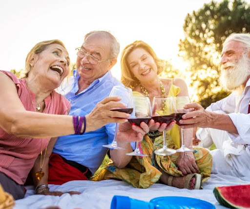 Two couples toast each other with wine outside.