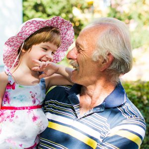 A man smiles while holding his granddaughter.