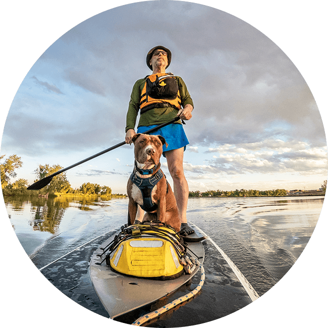 Guy outside enjoying his waterproof security hearing aid with his dog on a paddle board in the water