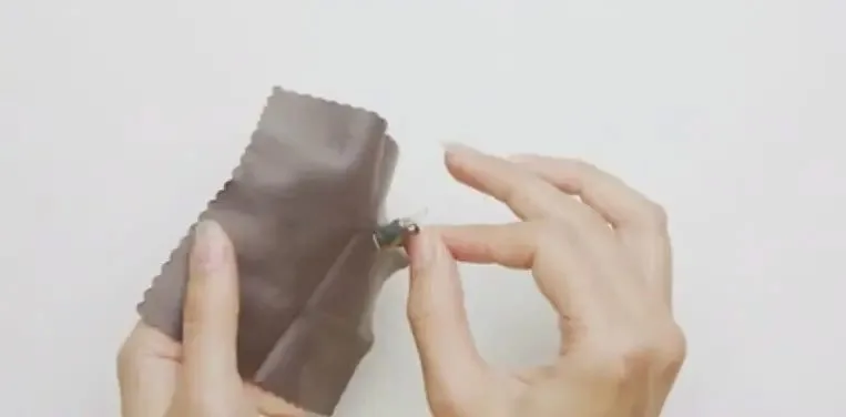 A hand uses a cloth to clean a Phonak hearing aid.