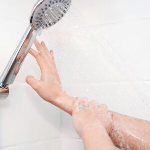 A woman's arm reaches for a shower head.