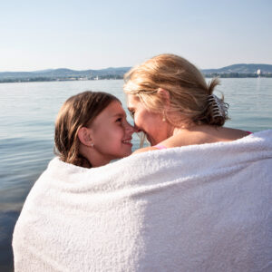A woman and her daughter cuddle after swimming.