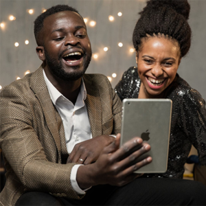 A couple laughs as they look at a tablet.