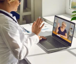 An audiologist waves at a patient during a telehearing appointment. 