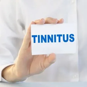 A white-coated person holds a card that says, “Tinnitus.”