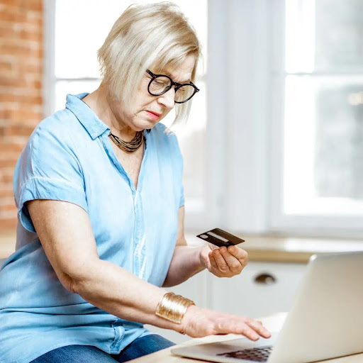 An older woman holds her credit card while buying hearing aids online.