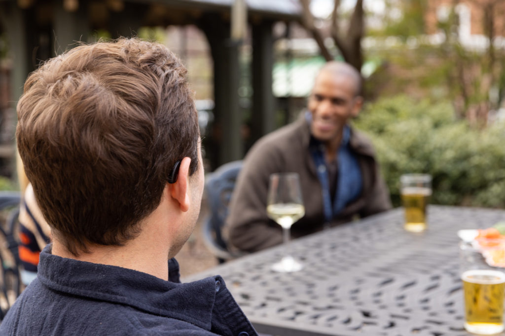 Man outside with hearing aid having a dinner table conversation