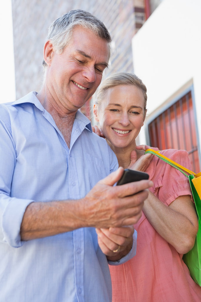 Happy senior couple looking at smartphone holding shopping bags