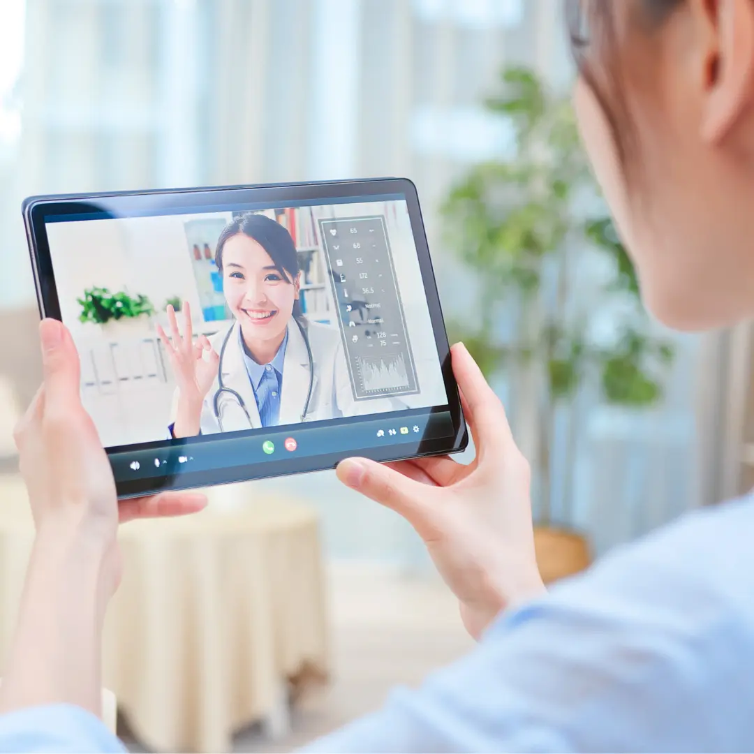 An audiologist waves at her patient on a tablet computer.