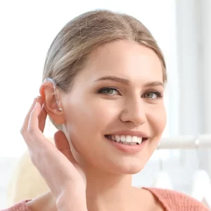 A woman smiles as she shows her hearing aid.