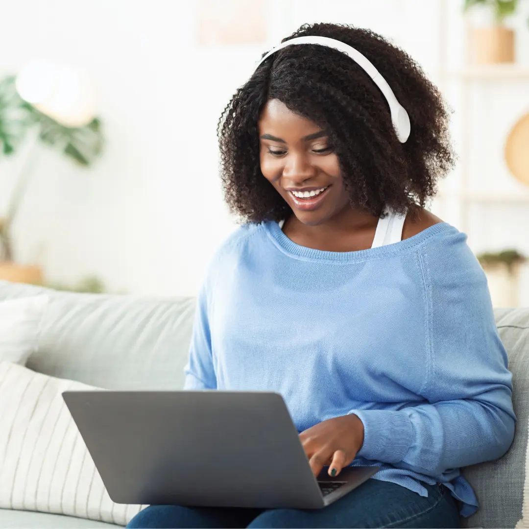 A woman with headphones smiles at her laptop screen.