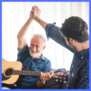 An older man high fives a younger man while playing guitar.