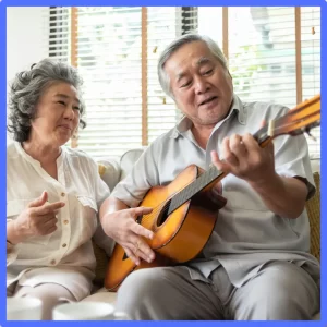 A couple sits together a sings while one plays the guitar. 