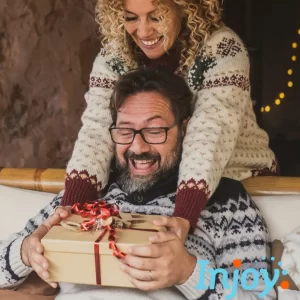 A man is ready to open a present from his wife, who stands behind him. 