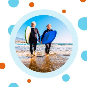 An older couple carries surfboards on the beach.