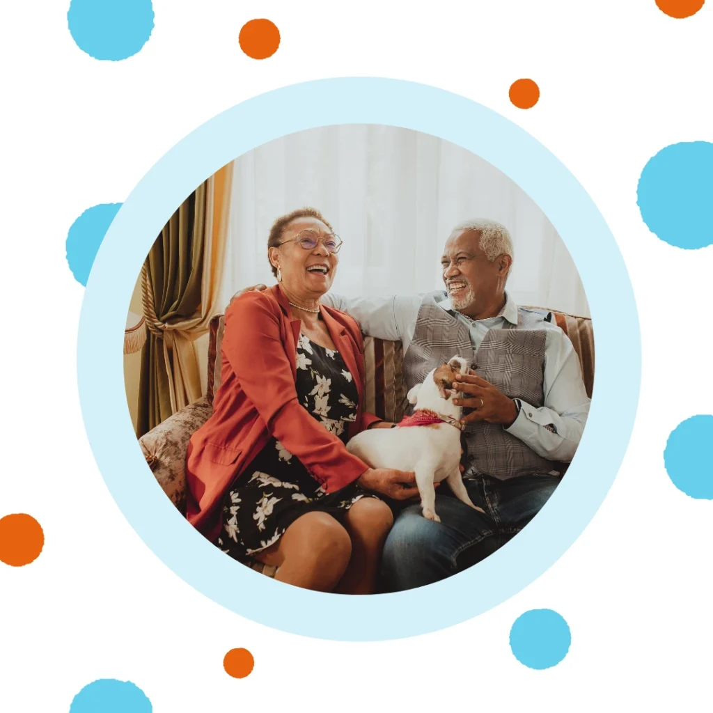 An older couple cuddles their dog on their couch.
