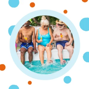 Older friends sit on the edge of a pool. 