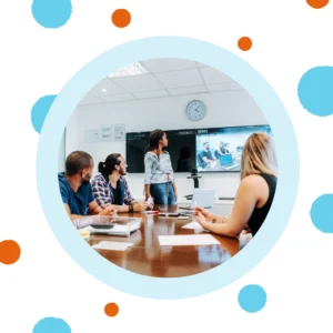 People sit around a conference table while one person speaks up front. 