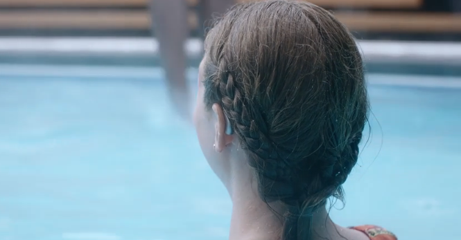 A woman with damp hair and a Phonak hearing aid stands beside a pool. 