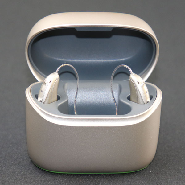 Silver Phonak hearing aids stand in their rechargeable case on a gray background. 