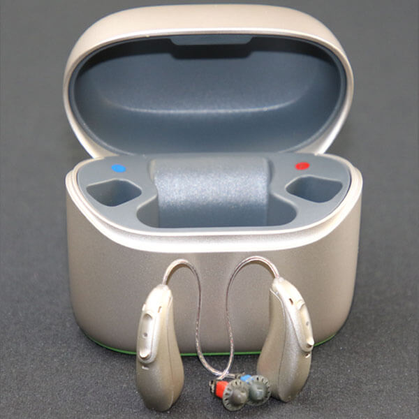 A pair of Phonak hearing aids stand in front of their charging case.