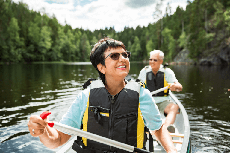 A smiling older couple canoes together on a pristine lake.