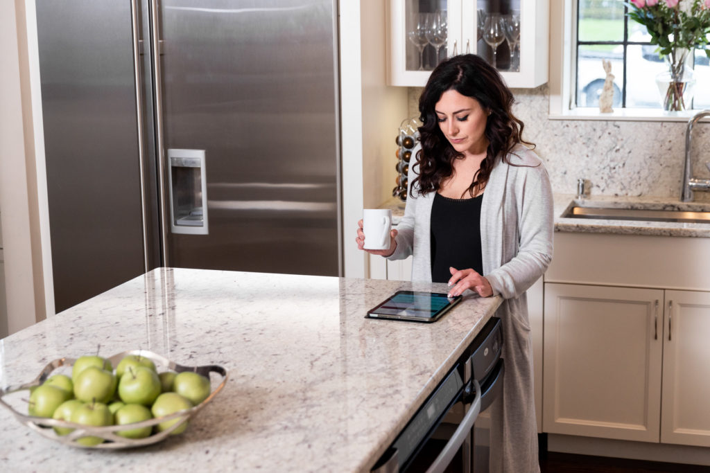 A woman drinks coffee in her kitchen while listening to her tablet.